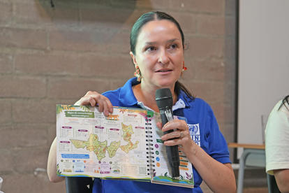 Photograph of a woman in a blue shirt presenting a calendar with maps, speaking into a microphone.