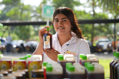 Photograph: smiling female vendor at an outdoor market with rows of green-labeled bottles.