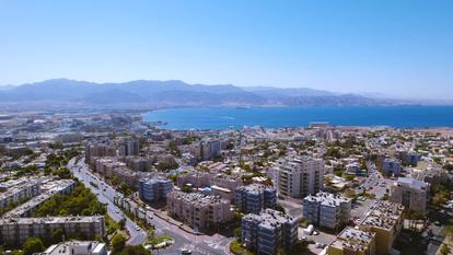 Aerial view of a coastal city with buildings, roads, and the blue sea on the horizon.