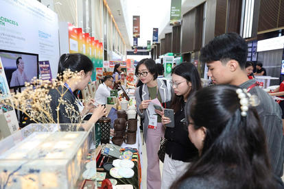 Group of people browsing wooden crafts, jars, and dried flowers at an indoor market fair.