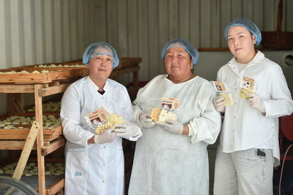 Photograph: Three people in lab coats and hairnets hold yellow-wrapped baked goods in a bakery.