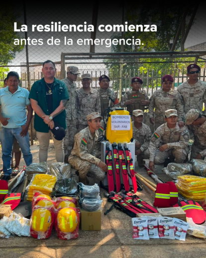 Military personnel and civilians pose with disaster relief gear and supplies outdoors.