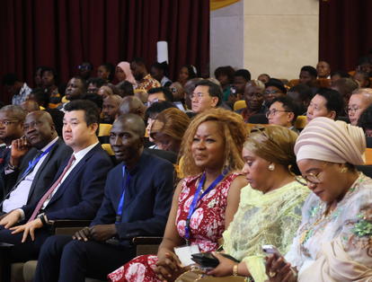 Diverse audience in formal attire seated in a conference hall, attentively watching.
