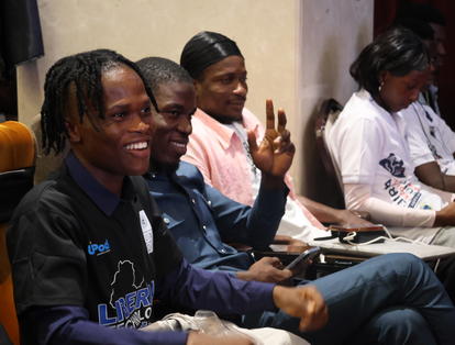 Five smiling men sit in a row at a workshop.