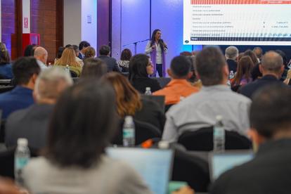 Speaker on stage delivering a talk to a crowded conference audience under blue lighting.