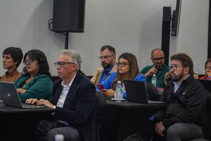 Photograph of conference attendees seated with laptops, listening to a presentation.