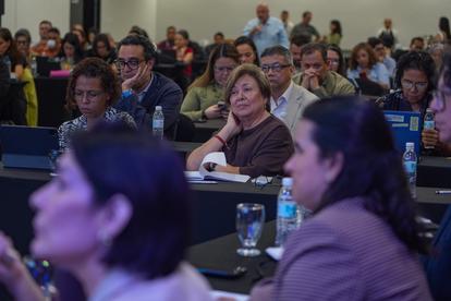Photograph of a conference audience seated at tables in a dimly lit room.