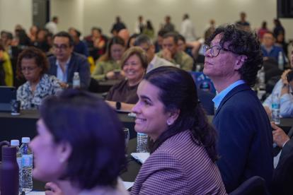 Photo: audience members seated in rows at a conference, listening attentively.