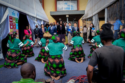 Group of dancers in green traditional costumes perform in a street, spectators watch.