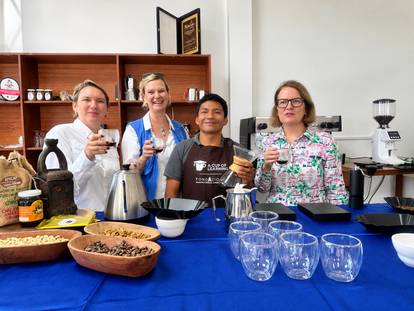 Four smiling people stand behind a blue table with cooking supplies, pies, and glassware.