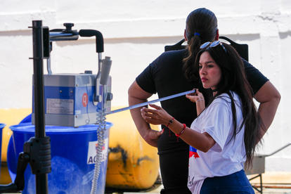 Photo of two people by a blue beverage cart on a beach boardwalk; woman holds a phone.