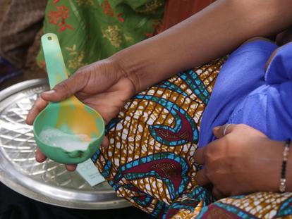 Person wearing bright patterned fabric holding a green and yellow cup beside a metal plate.