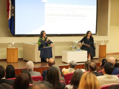 Two women on stage at a panel in a lecture hall, projection screen behind them.