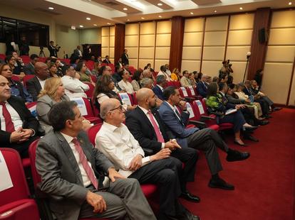 Photograph of an audience seated in rows inside a wood-paneled conference hall.