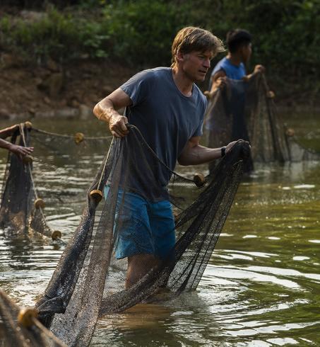Four people working together to fish in a calm river, surrounded by lush greenery.