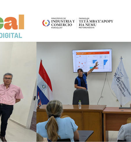 Group photo of participants and speakers at a local event, with flags and presentation screens.