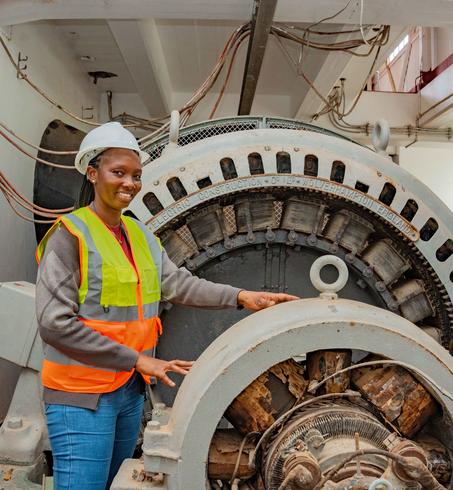 Photograph of a worker in hard hat and high-vis vest beside a large industrial generator.