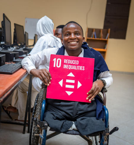 Smiling man in a wheelchair holds pink SDG 10 sign about reduced inequalities.