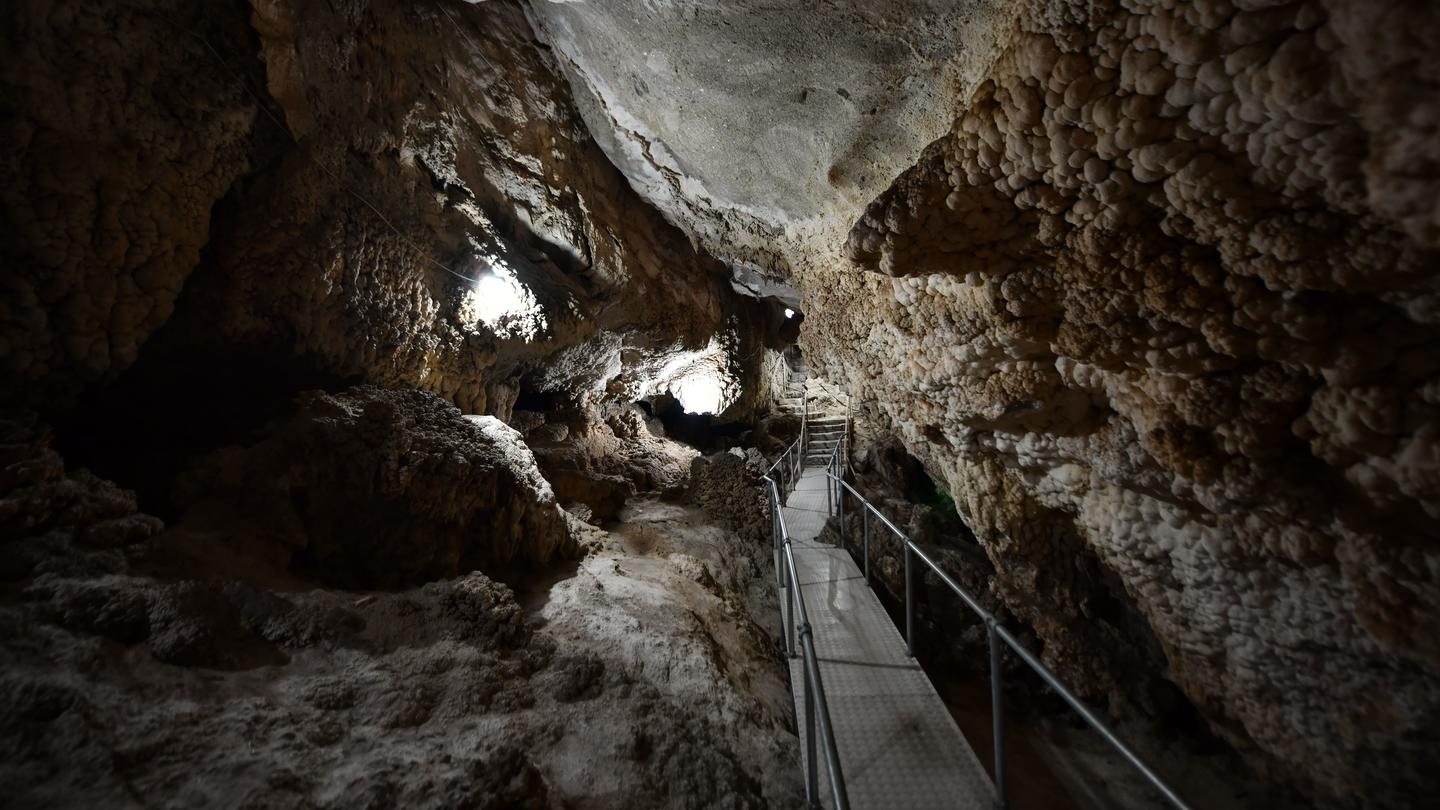 Dimly lit cave interior with rock formations and a metal walkway.