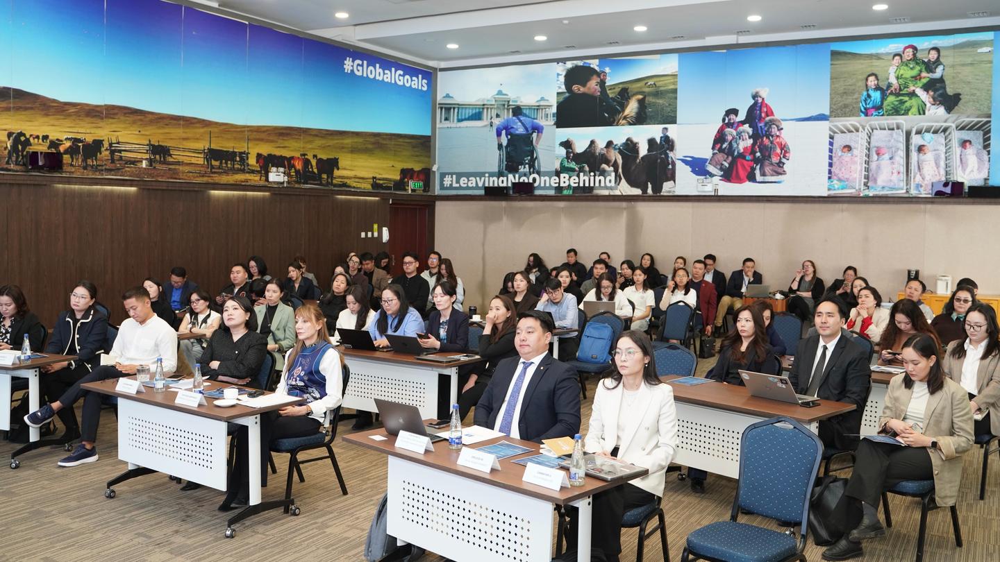 A diverse group of people seated in a conference room, engaged in a meeting or presentation.
