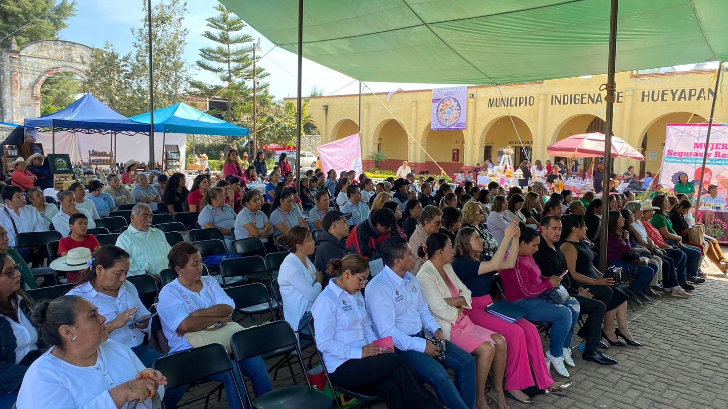 A large crowd seated under a green canopy, engaged in an outdoor event.