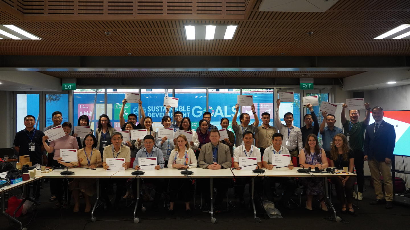 A diverse group of individuals holding certificates, gathered around a table in a conference room.