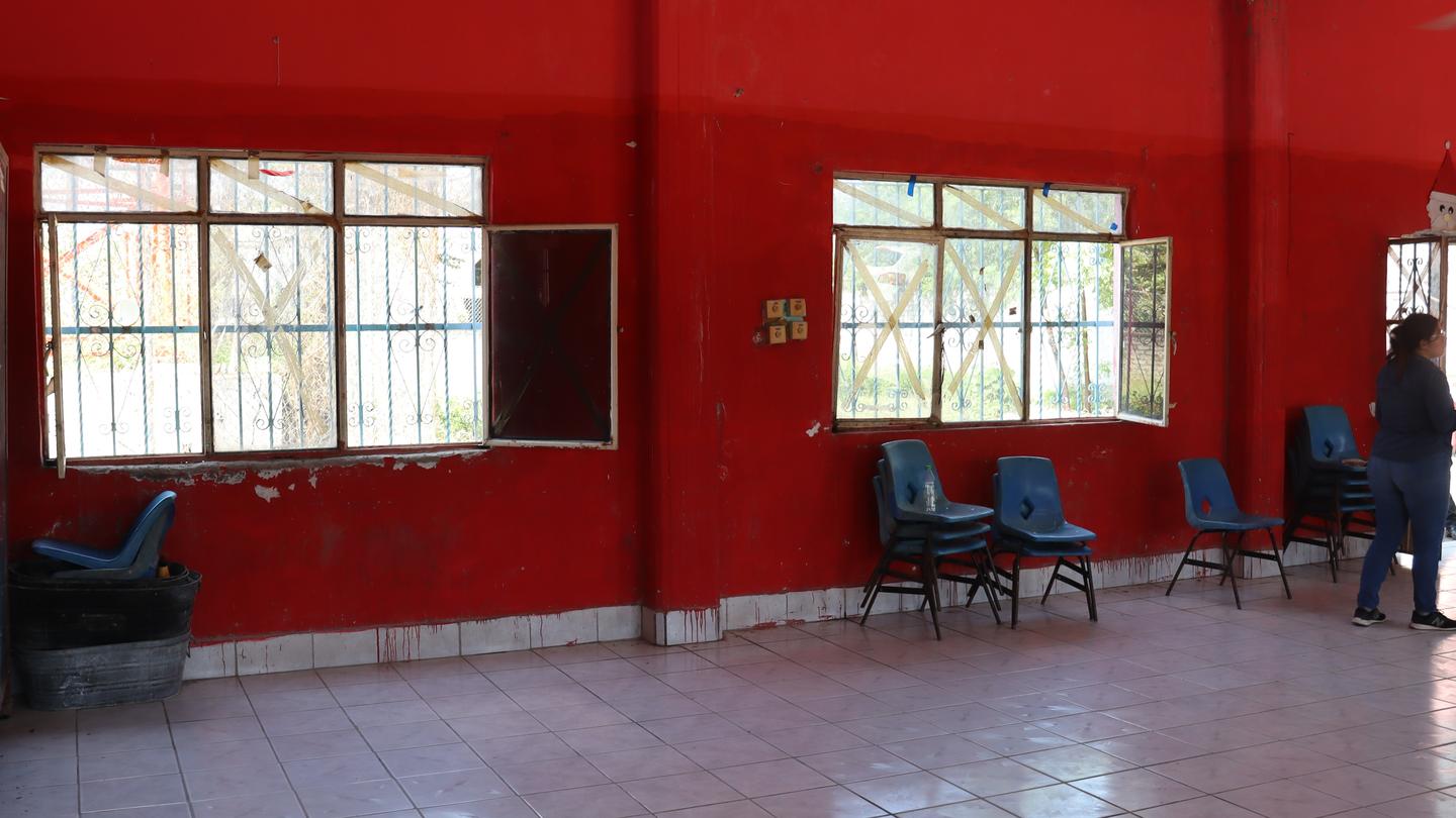Interior of a red-walled room with empty blue chairs and a person standing by a window.