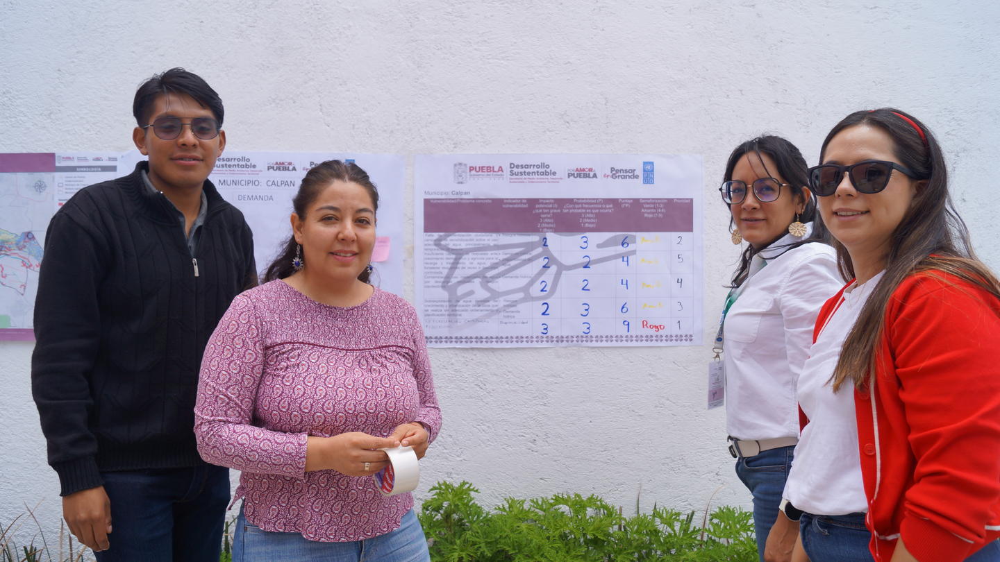 Four people stand in front of a wall displaying maps, smiling and engaged in conversation.