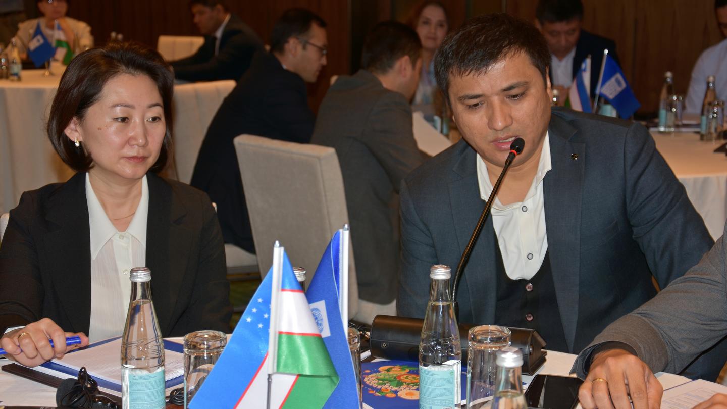 Photograph of conference attendees around a table with flags, papers, and water bottles.