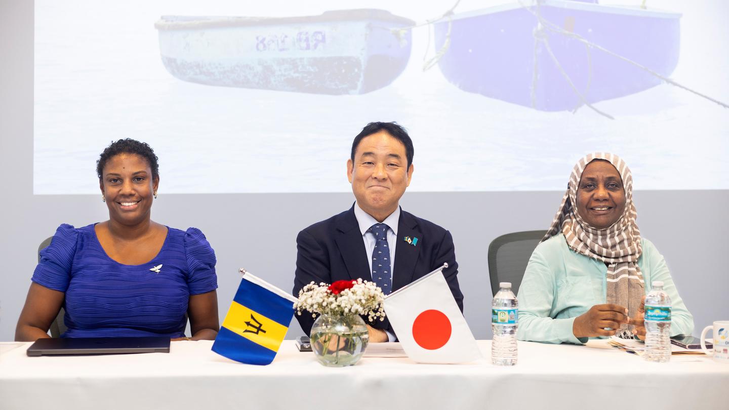 Three officials sit at a conference table with Japan and Rwanda flags.