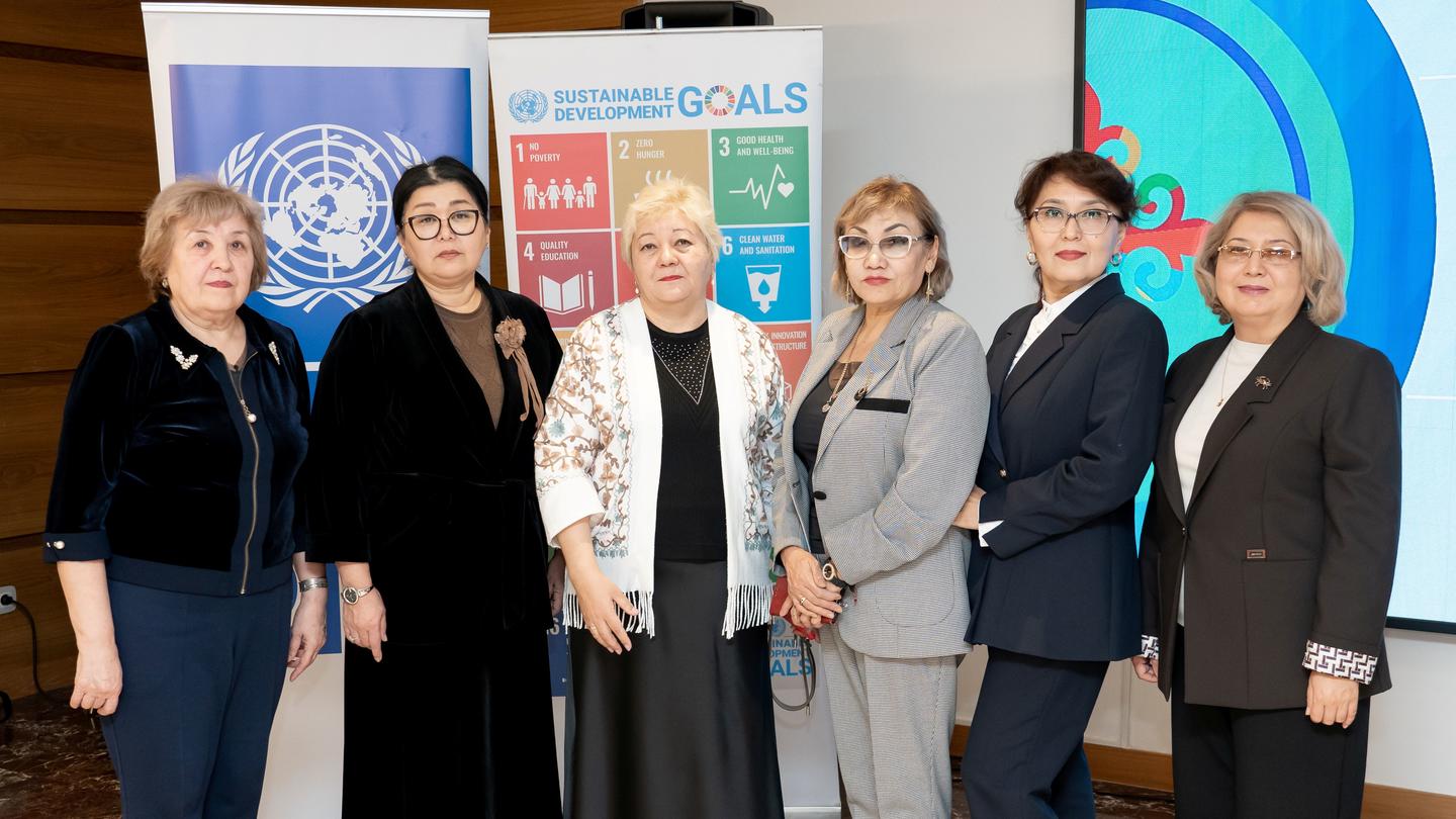 Group of smiling women in business attire pose in front of UN and SDG banners at a conference.