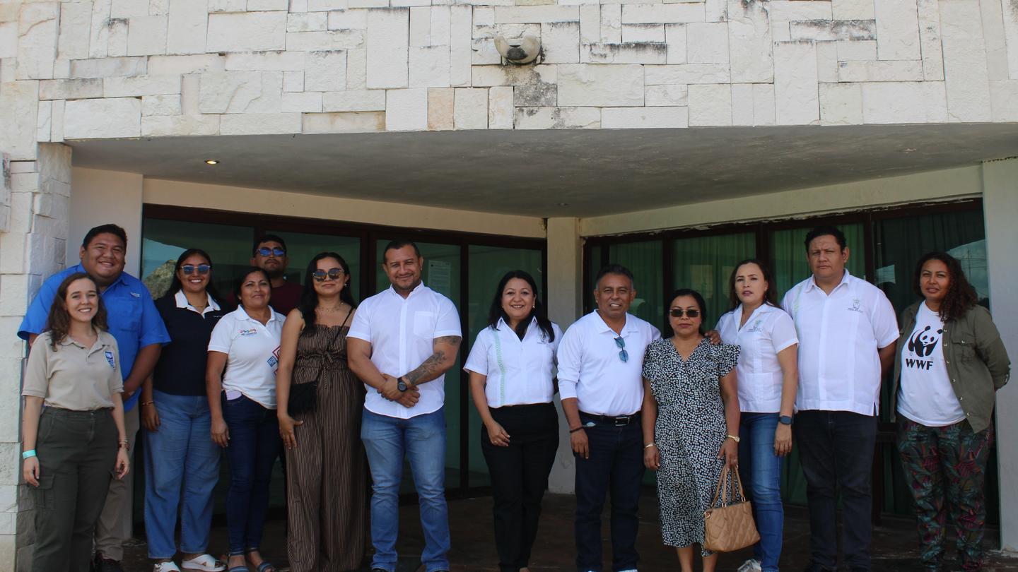 Group of people standing in a row outside a light stone building, posing for a photo.