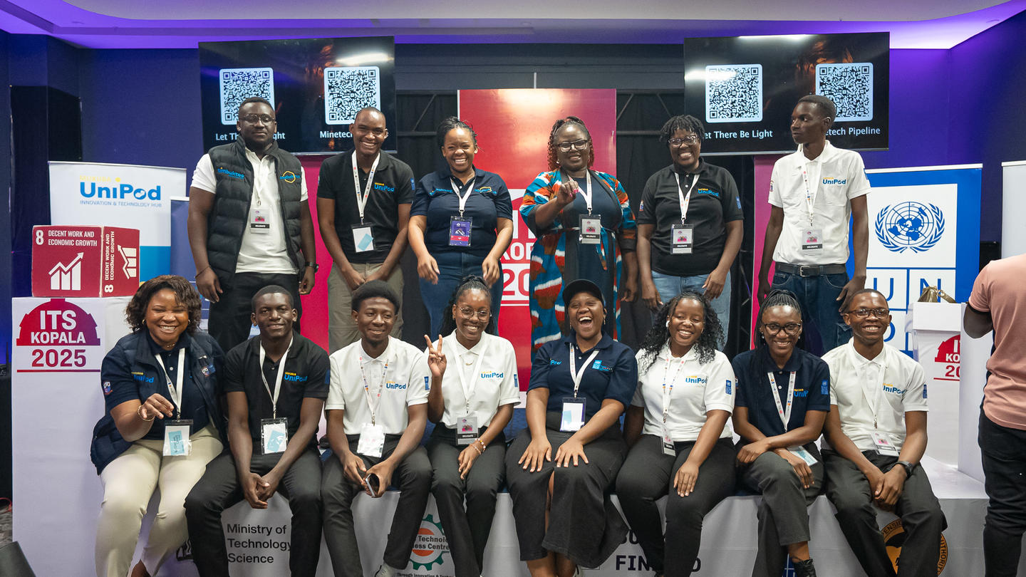 Photo: diverse group with lanyards posing on a purple-lit conference stage.