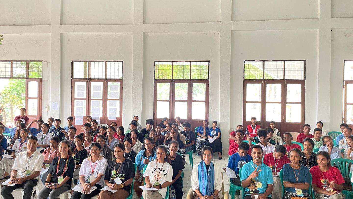 Large group of people seated in a bright hall, posing for a group photo.