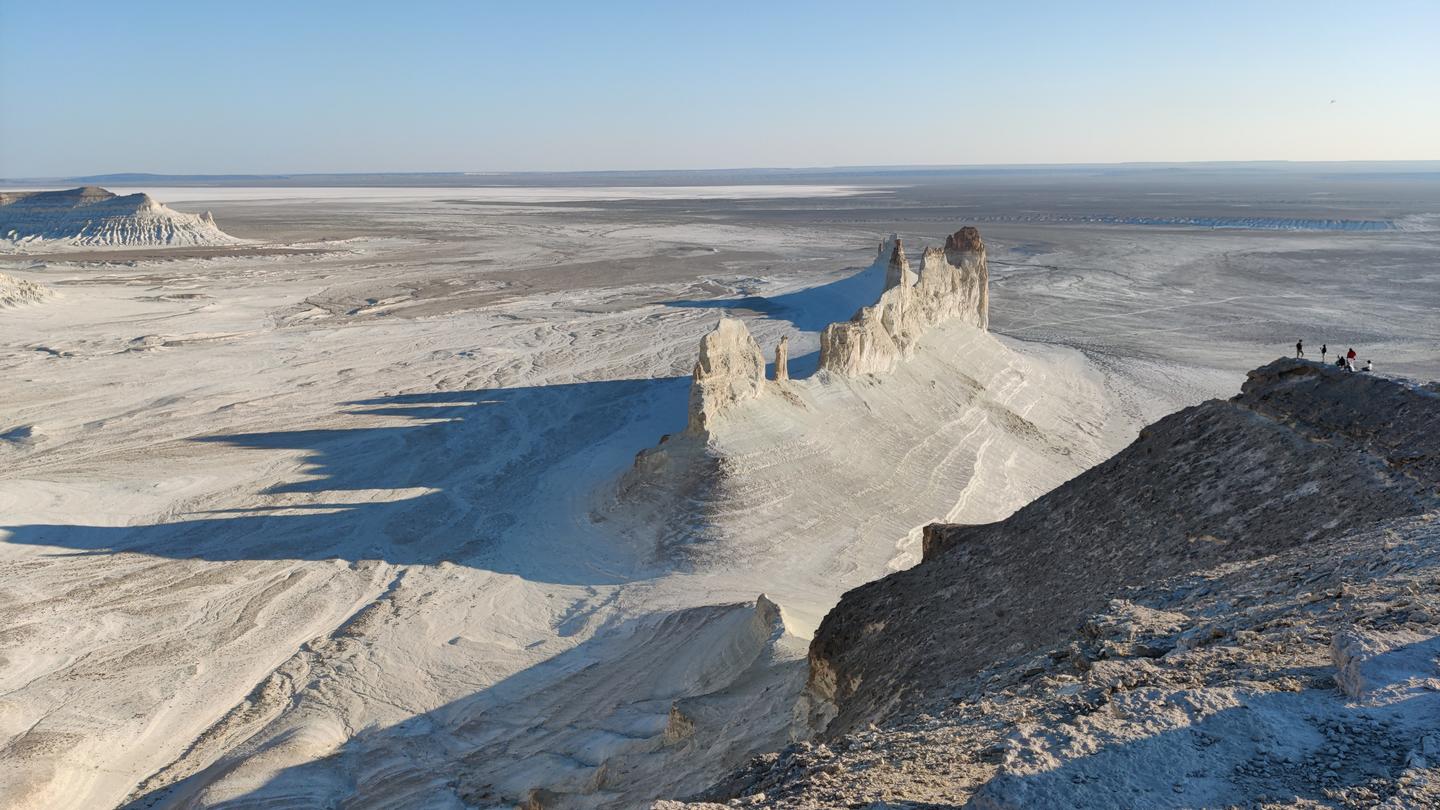 Desert landscape with white gypsum dunes, rocky ridge, and a clear blue sky.