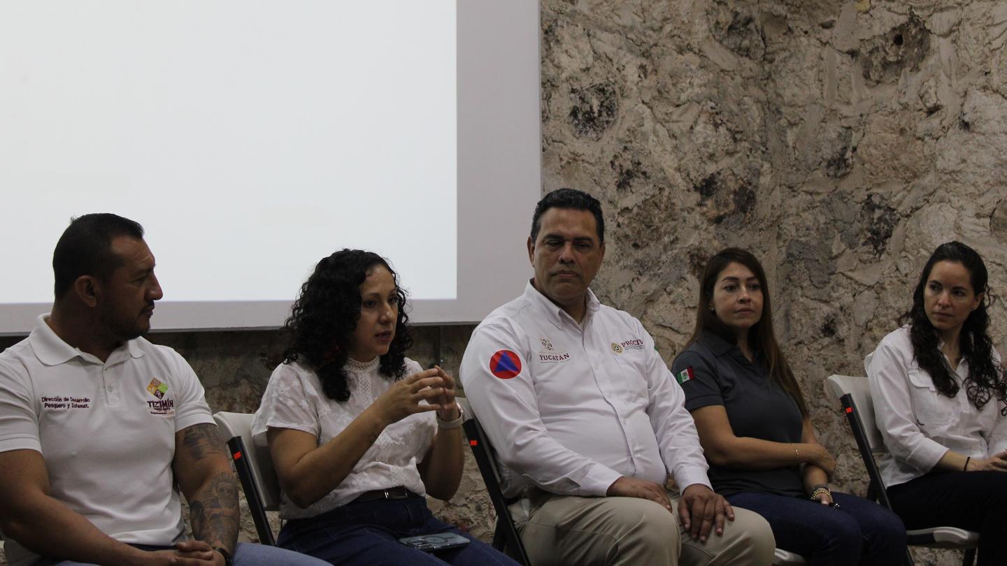 Five panelists seated on a stage against a stone wall during a discussion.