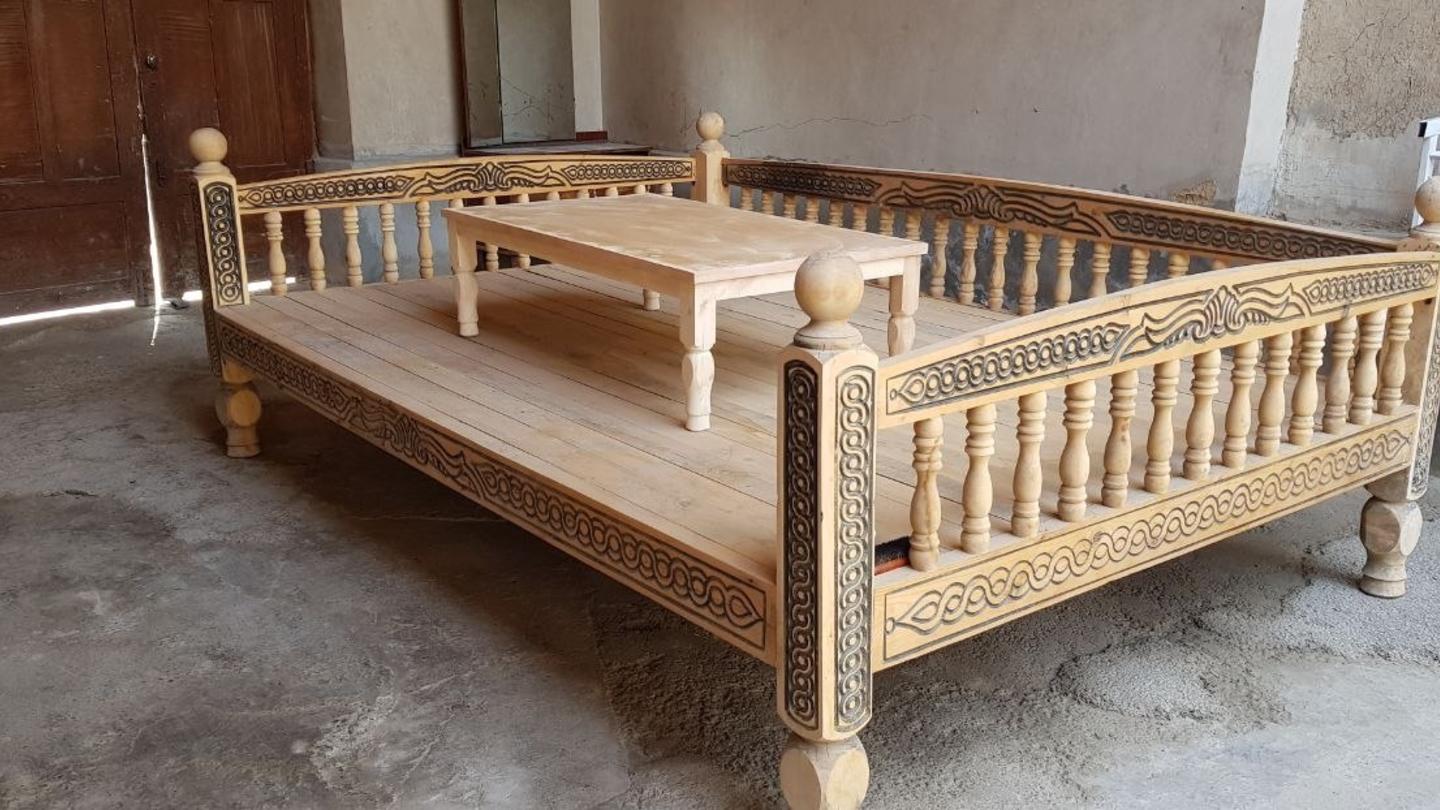 Wooden four-poster bed frame with carved posts in a workshop.