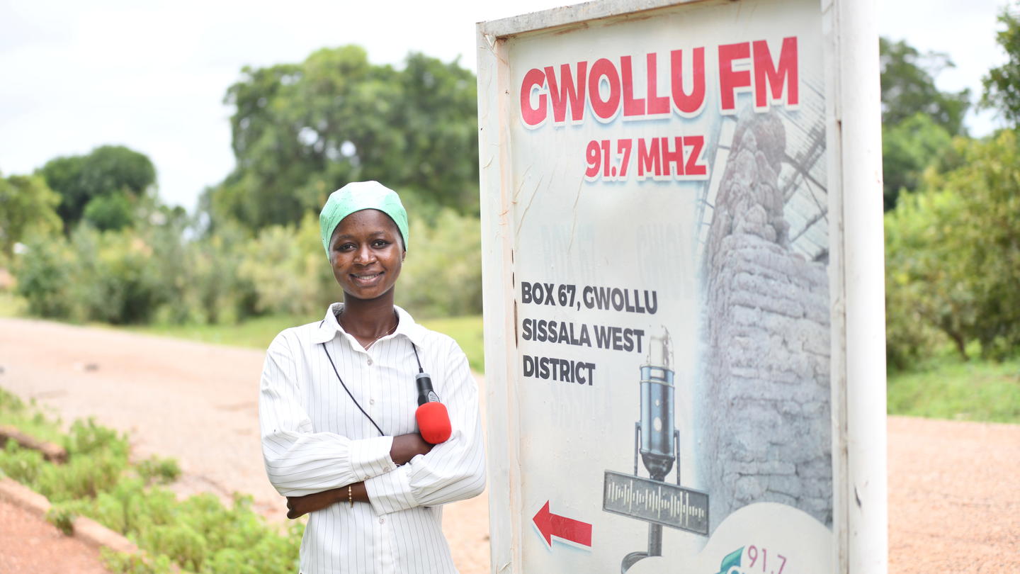 Man in white shirt beside a roadside billboard advertising FM radio at 97 MHz in a rural setting.