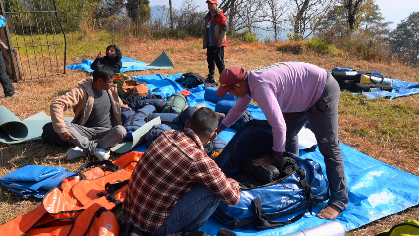 Group of people outdoors on a grassy field, sorting orange life jackets on blue tarps.
