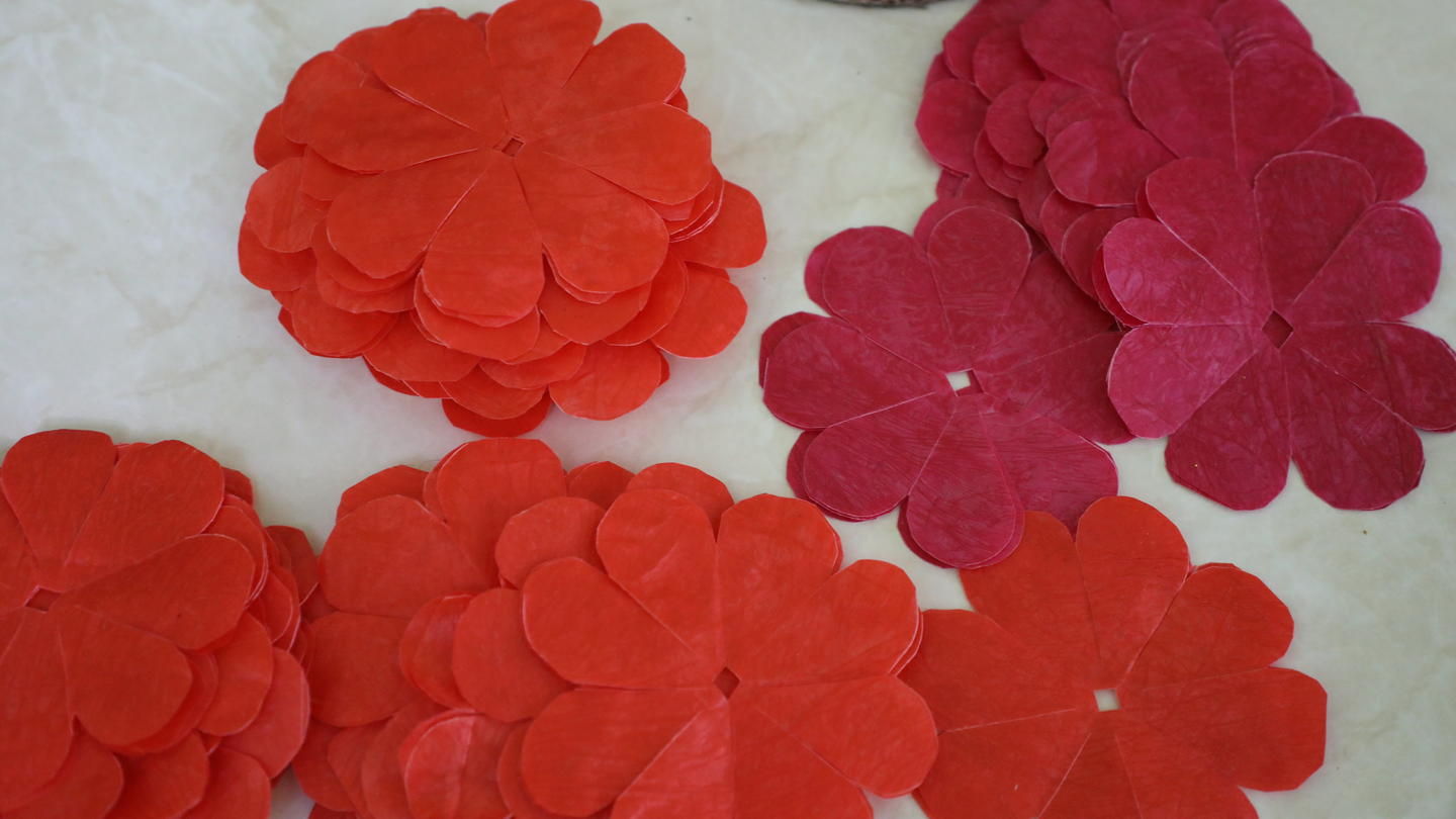 Cluster of red, pink, and orange layered paper flowers on a light surface.