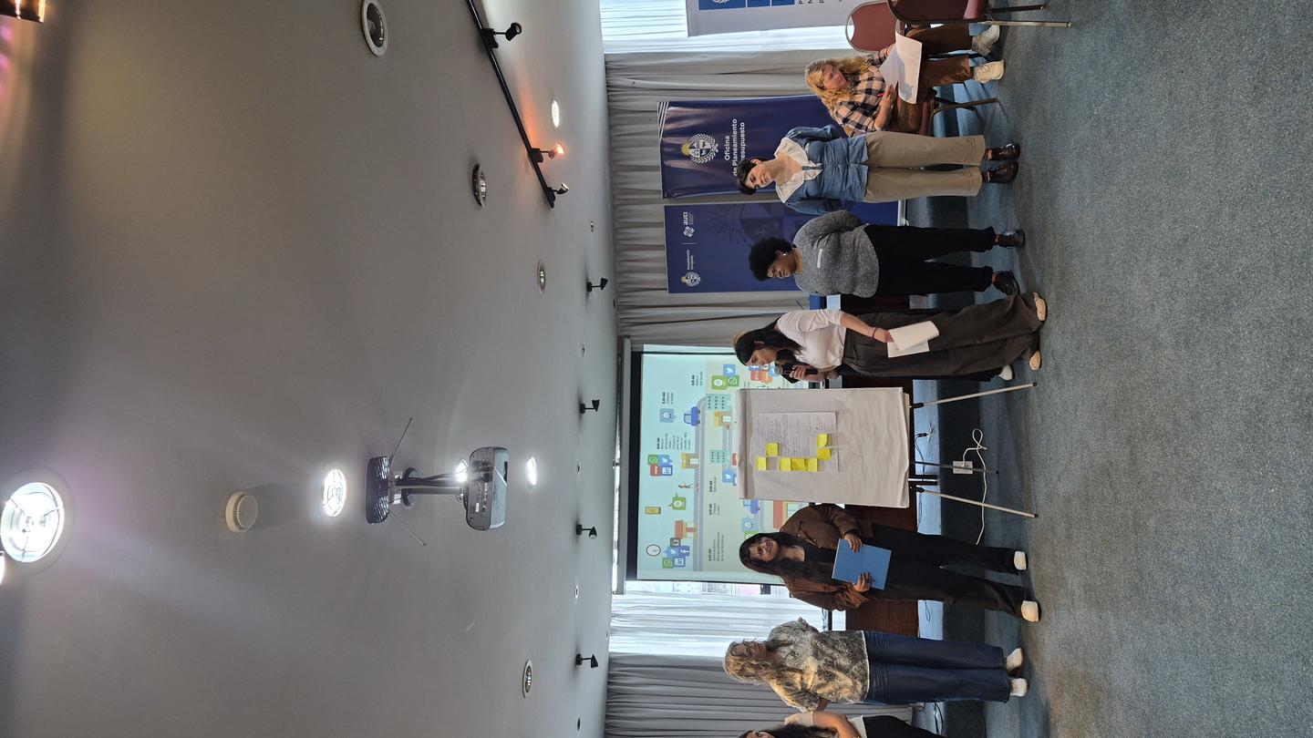 Group photo in a conference room with blue curtains and a projector screen.