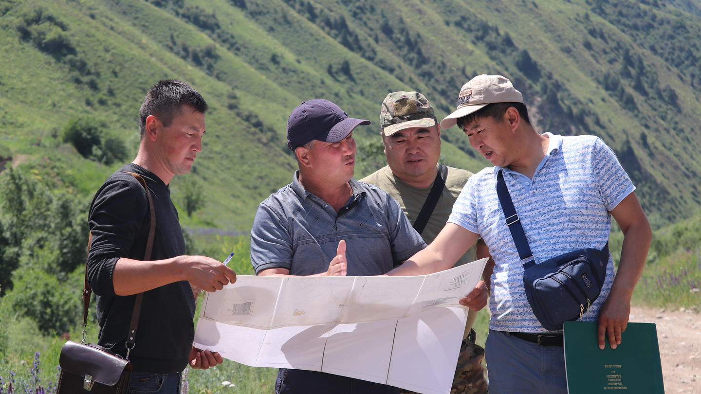 Group of four men outdoors on a hillside examining a large map.