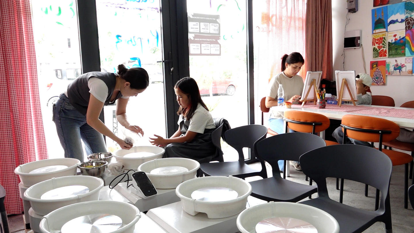 Photograph of students in a bright classroom gathered around round tables with bowls.