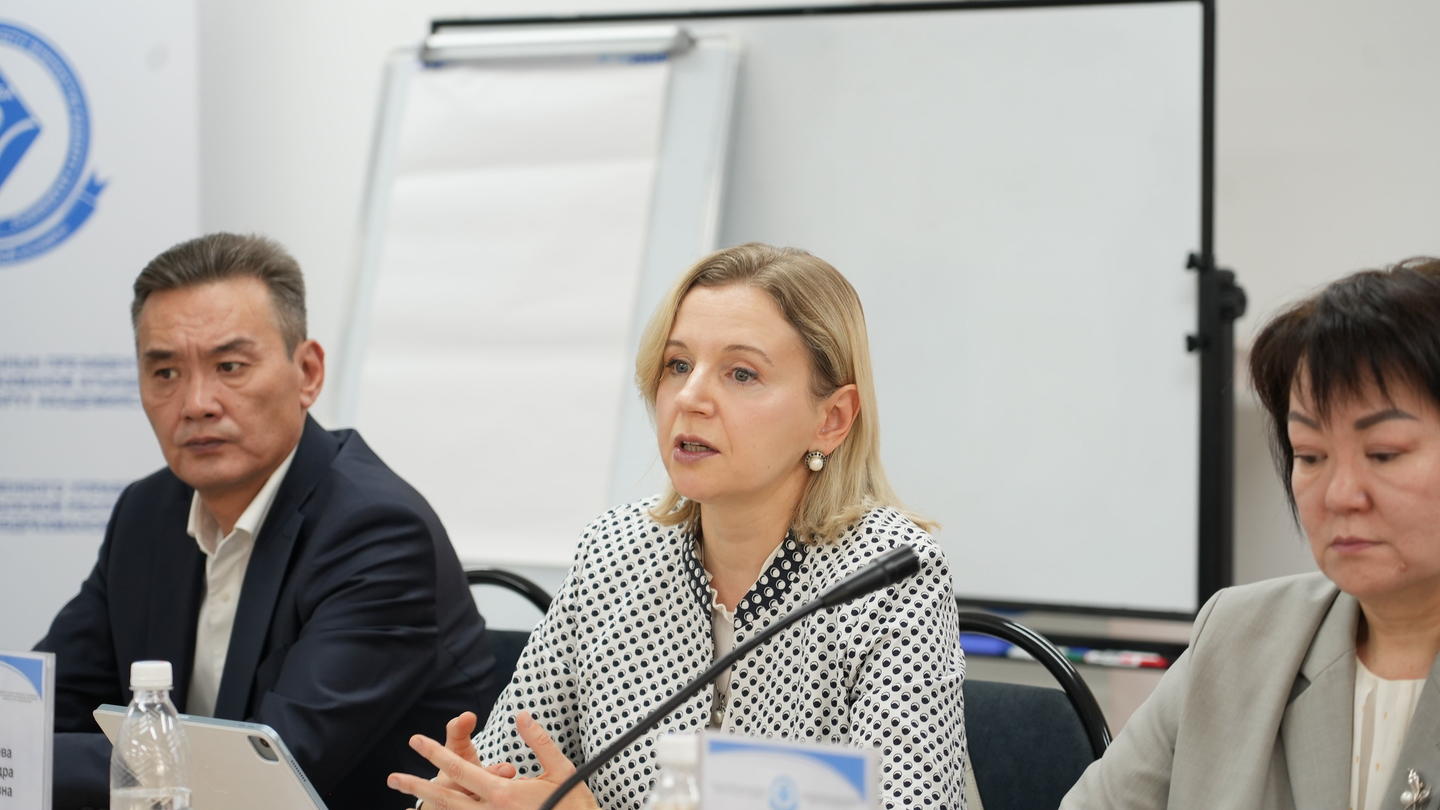 Three panelists at a conference table with name tags, speaking.