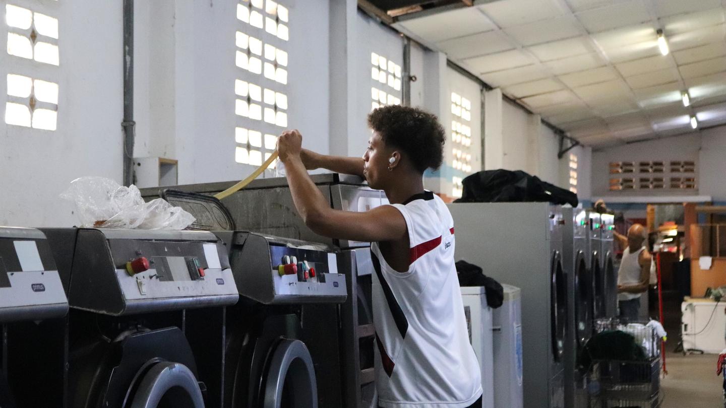 Young man loading clothes into front-loading washers in a bright laundromat.