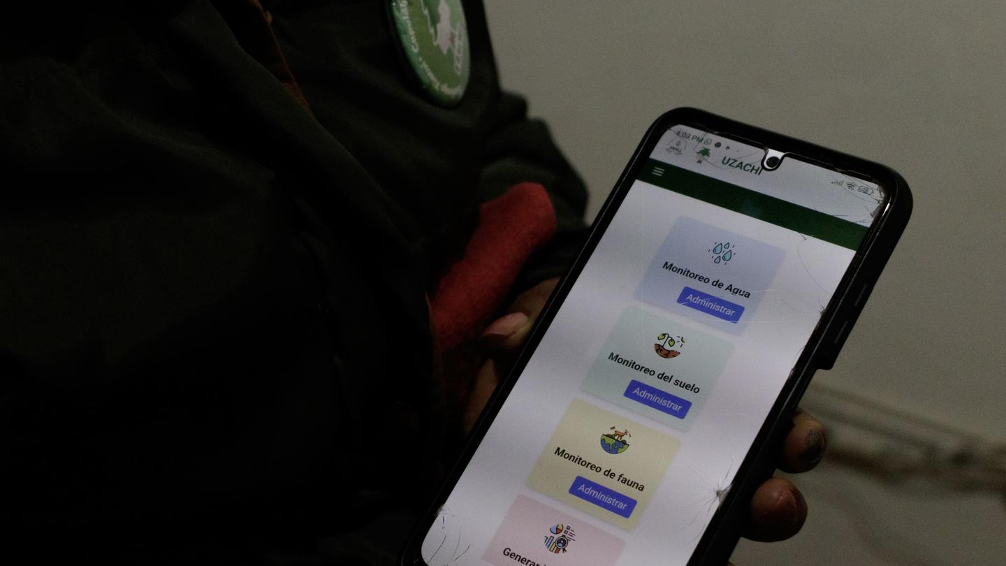 Person in a dark jacket with a green badge holds a smartphone displaying a colorful app.