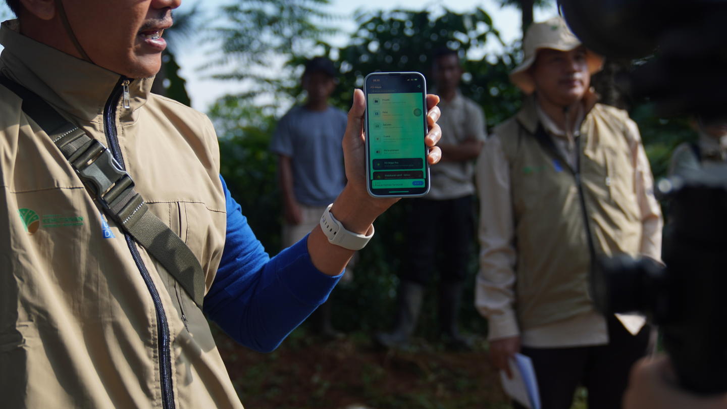Park rangers outdoors; foreground person in tan uniform holds up a smartphone with a green screen.