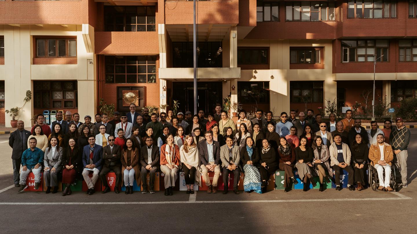 Large group of students and teachers posing in front of a brick school building.