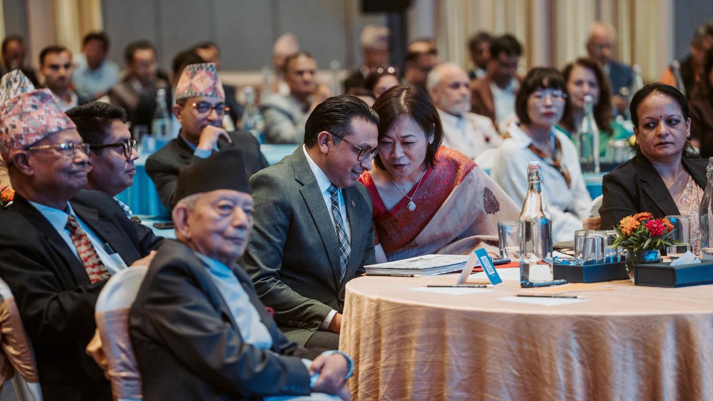 Photograph: Guests at a formal banquet sit at round tables; a teal-suited man chats with a woman in purple.