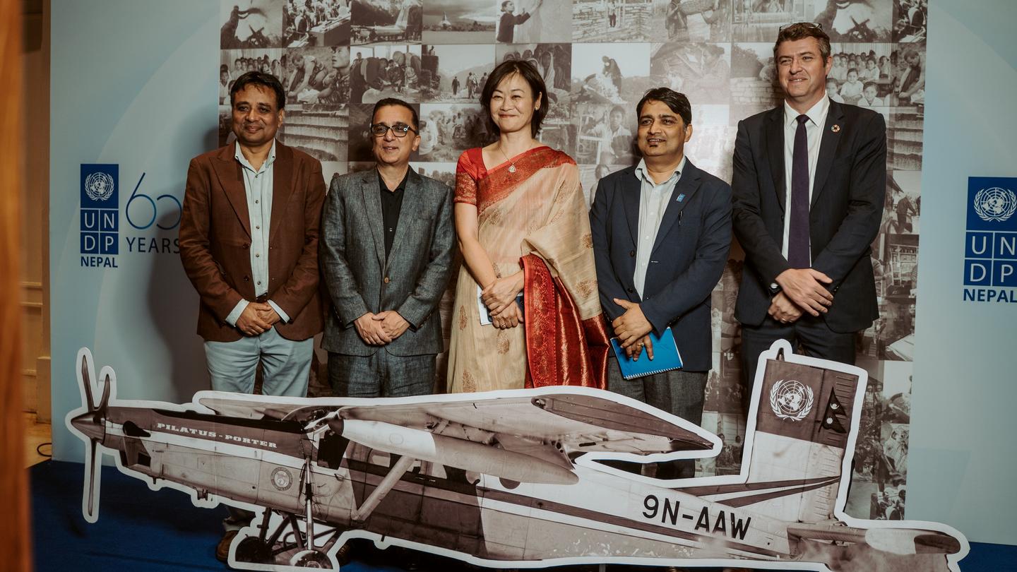 Five people pose behind a vintage airplane cutout on a blue backdrop with event logos.